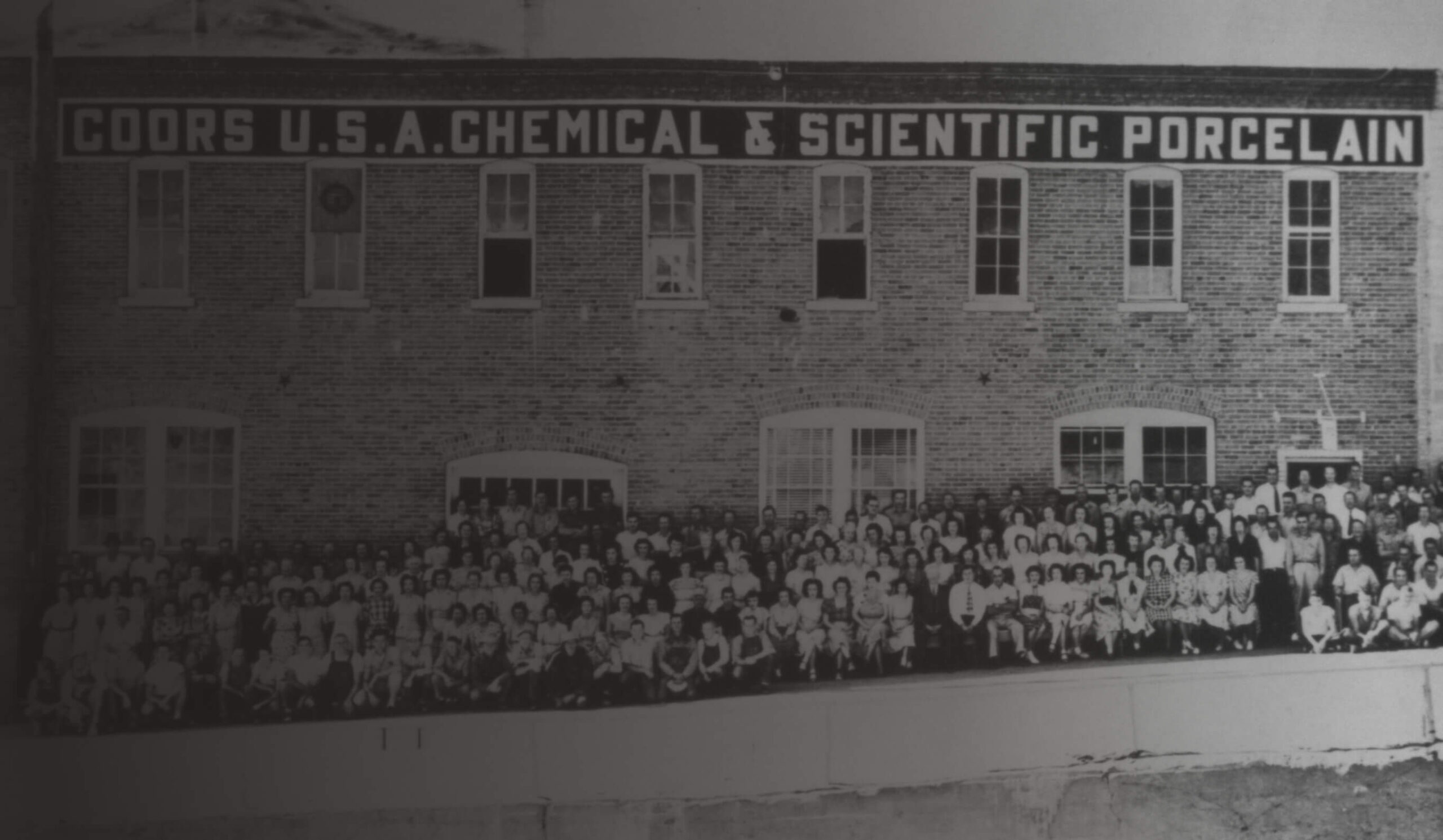 A black and white image of Coors Porcelain Company employees standing outside of the Coors Porcelain Company building.