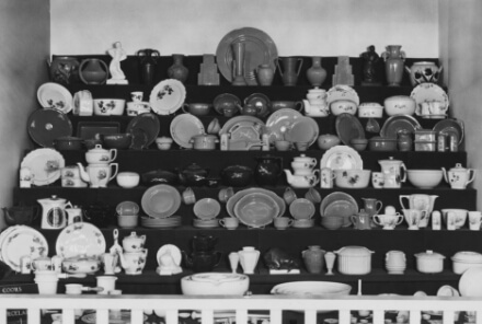 A black and white image of a shelf with Coors Porcelain dinnerware.
