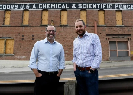 Dan Cohen and Michael Coors standing in front of the Coors Porcelain Company building.